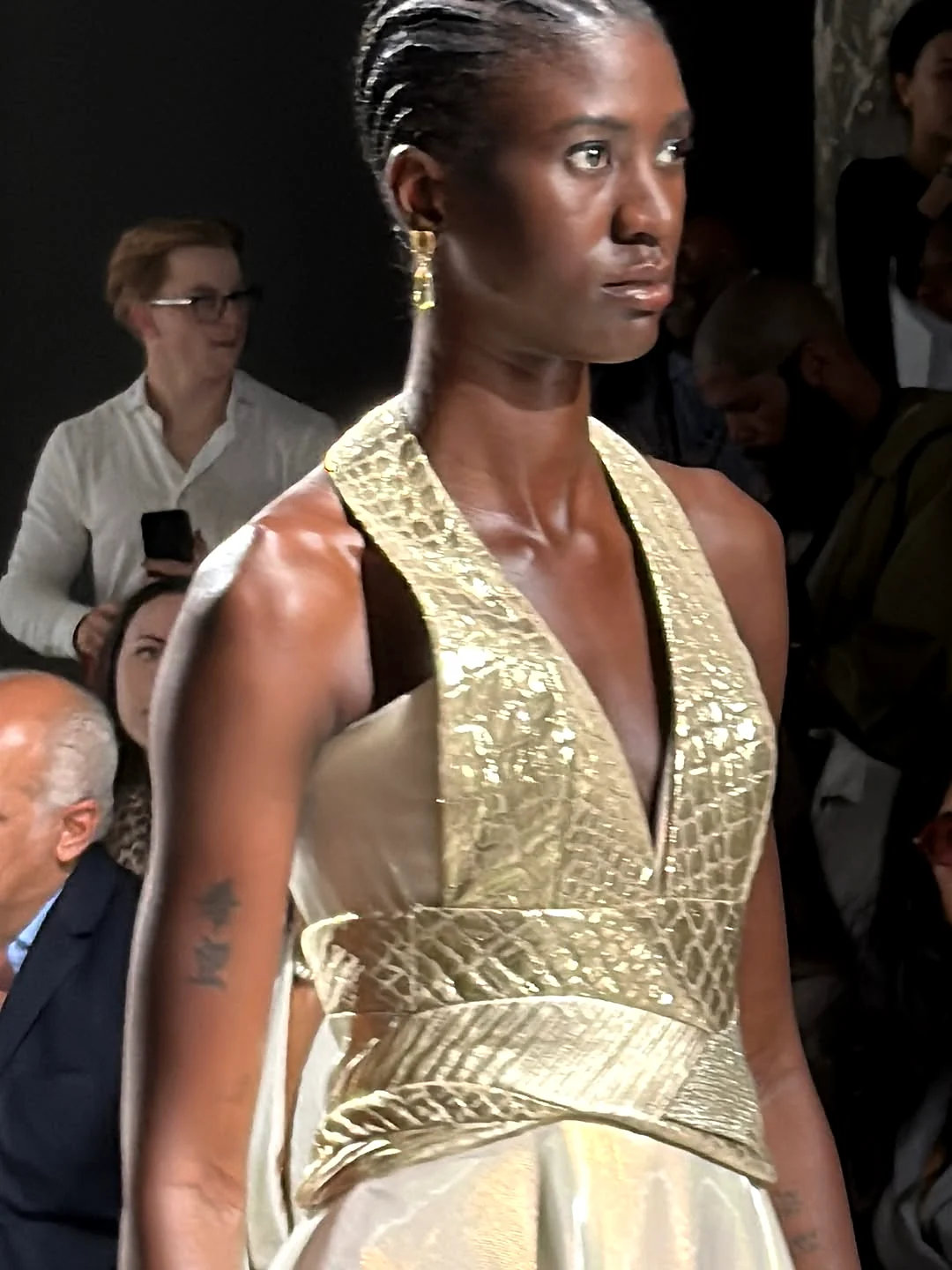 Closeup af model med glødende hud, defineret makeup og guldøreringe på catwalken